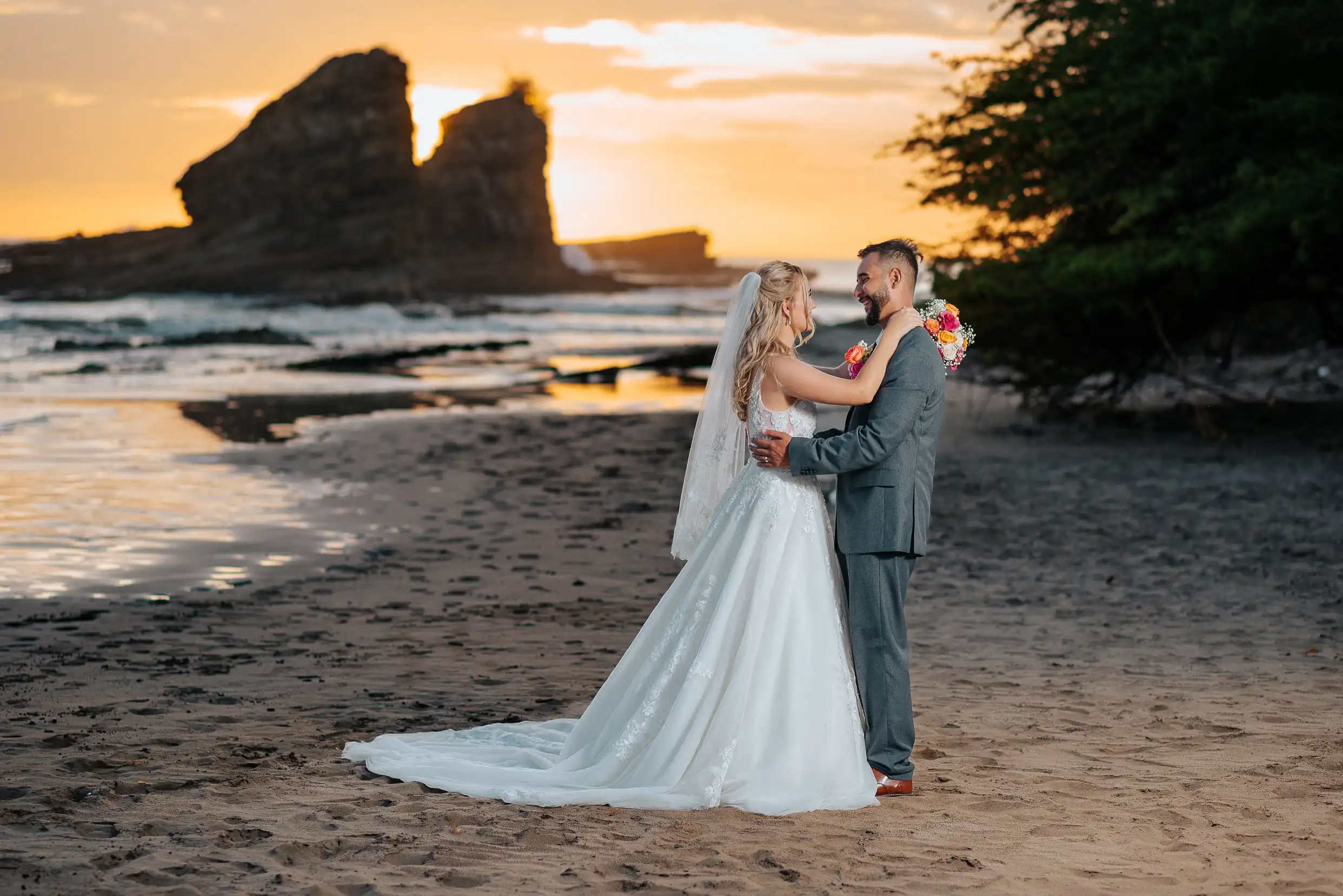 Bride and groom embracing on the beach at sunset with the iconic Magnific Rock sea in Popoyo, Nicaragua
