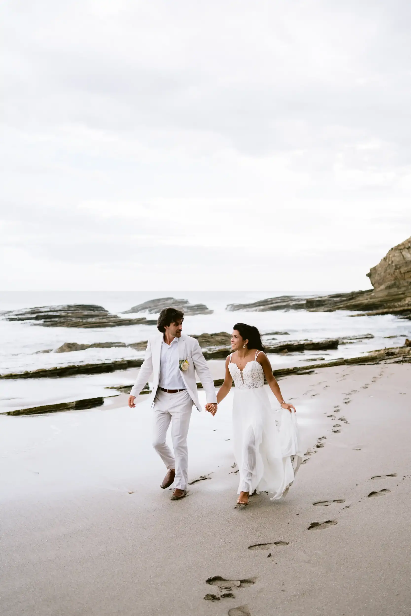 Bride and groom walking hand in hand along the sandy beach at Magnific Rock in Popoyo, Nicaragua