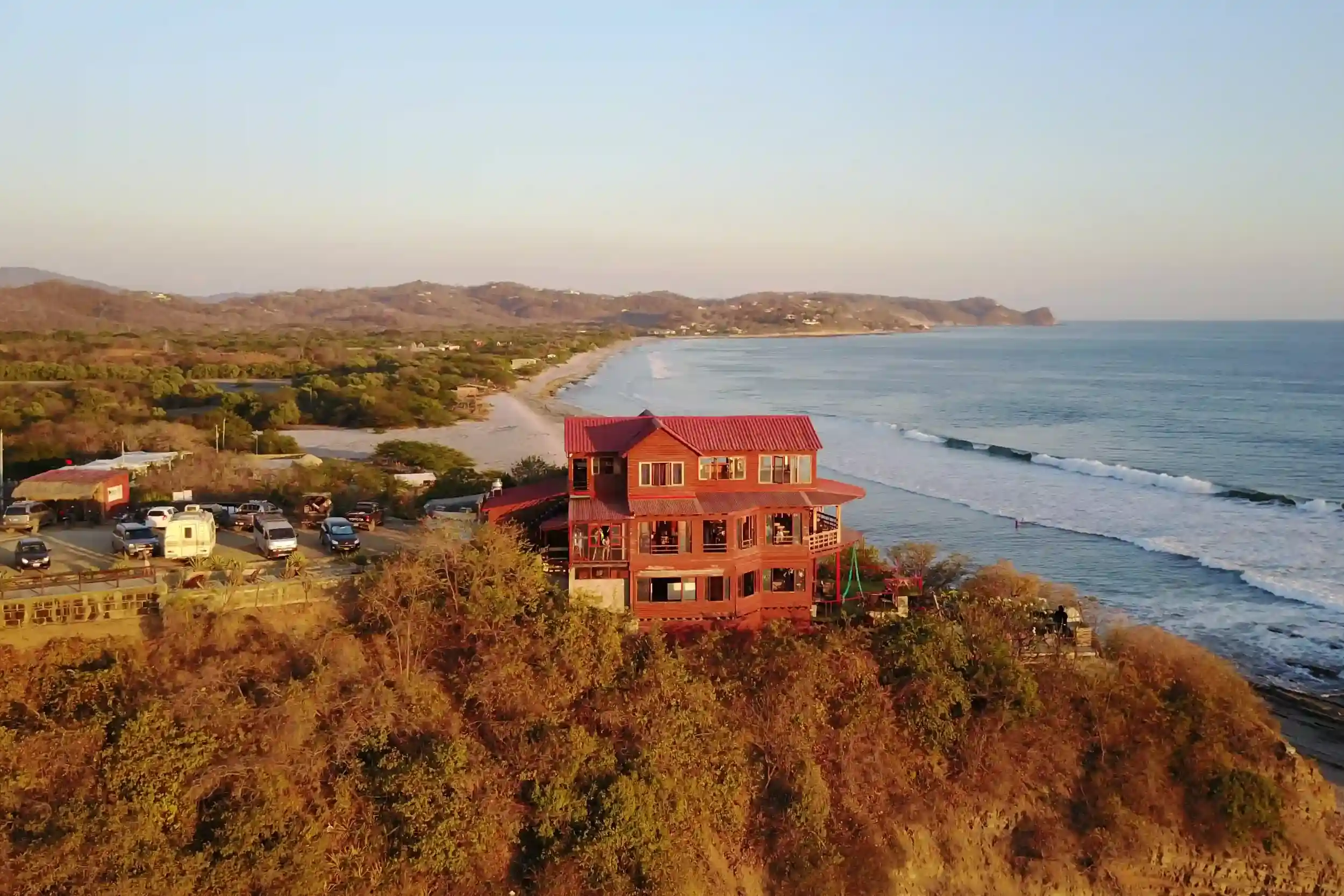Aerial view of Magnific Rock perched on a cliff above the Pacific Ocean in Popoyo, Nicaragua showcasing the oceanfront retreat setting with rolling waves, sandy